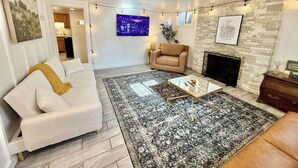 Un salon avec un canapé blanc, un fauteuil beige, une table basse et une cheminée.