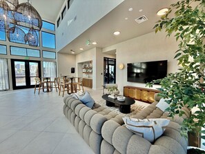 A spacious living area with a large sectional sofa, a dining table with chairs, a flat-screen TV, and a large window overlooking the outside. - Luxury Sandbar Oasis | Pool + Private Hot Tub (Washington)