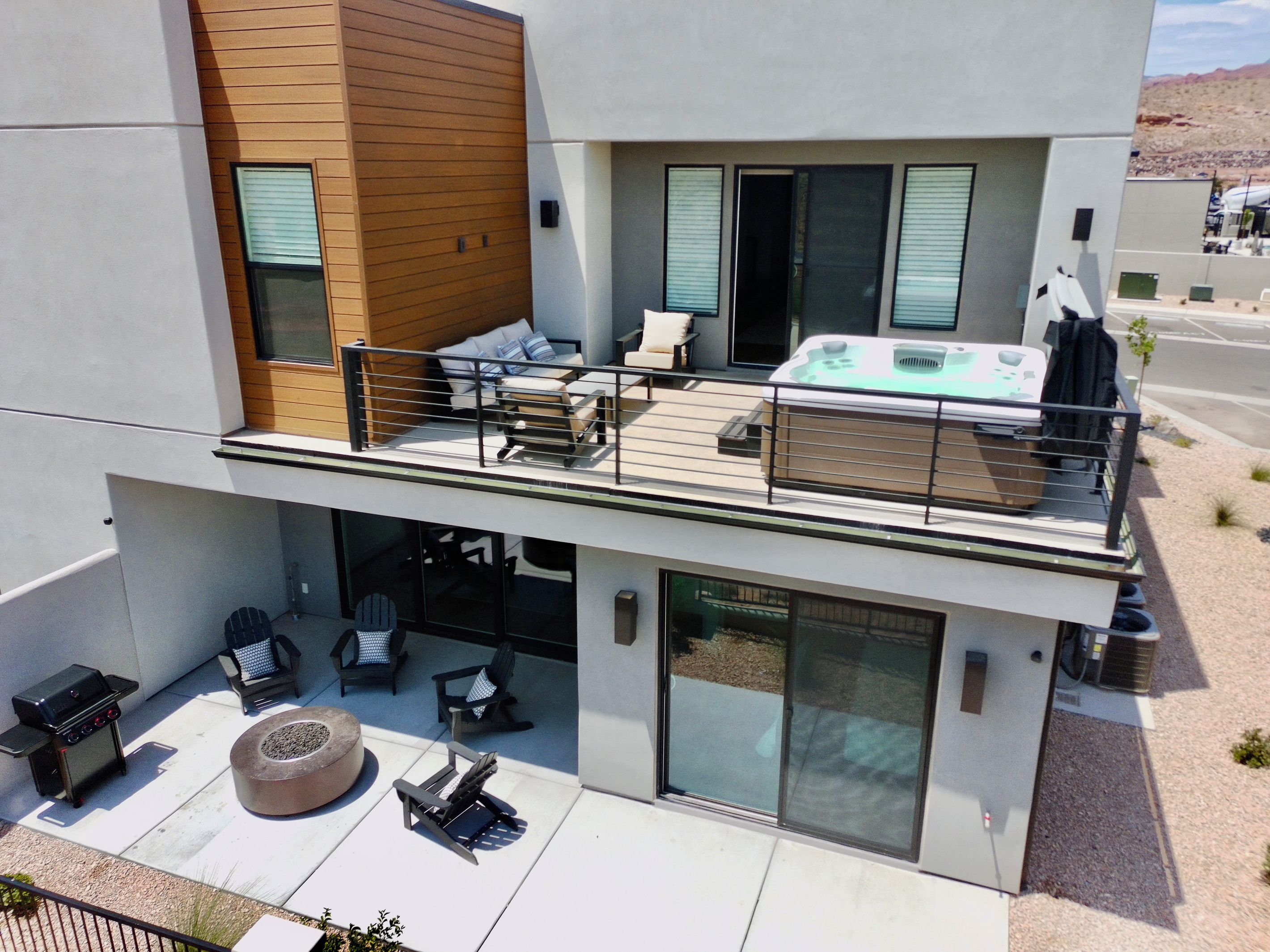Un edificio moderno de dos pisos con terraza en el techo, mobiliario exterior y un jacuzzi.