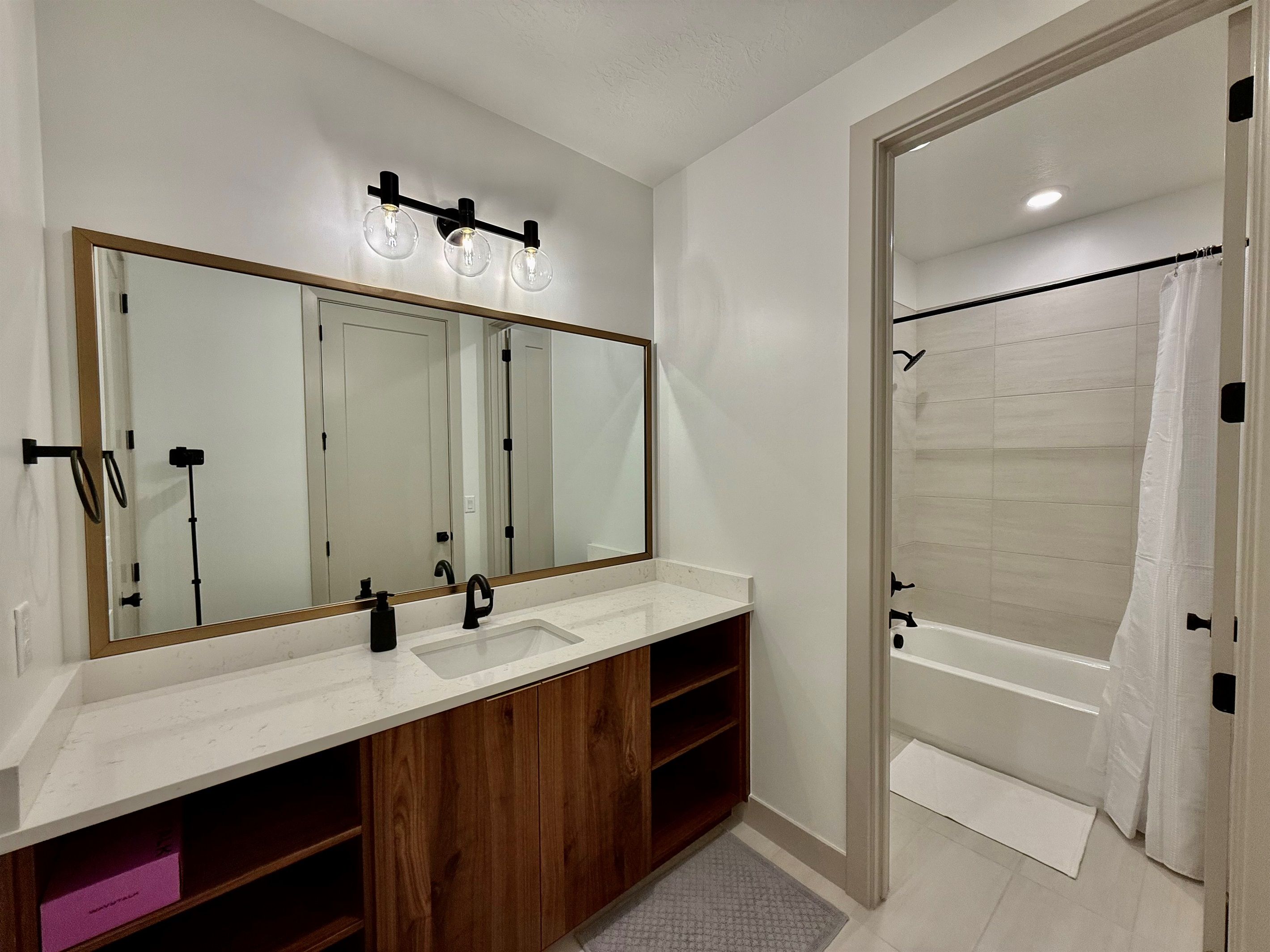 A bathroom with a large mirror, a sink, a shower, and a vanity with wooden cabinets.