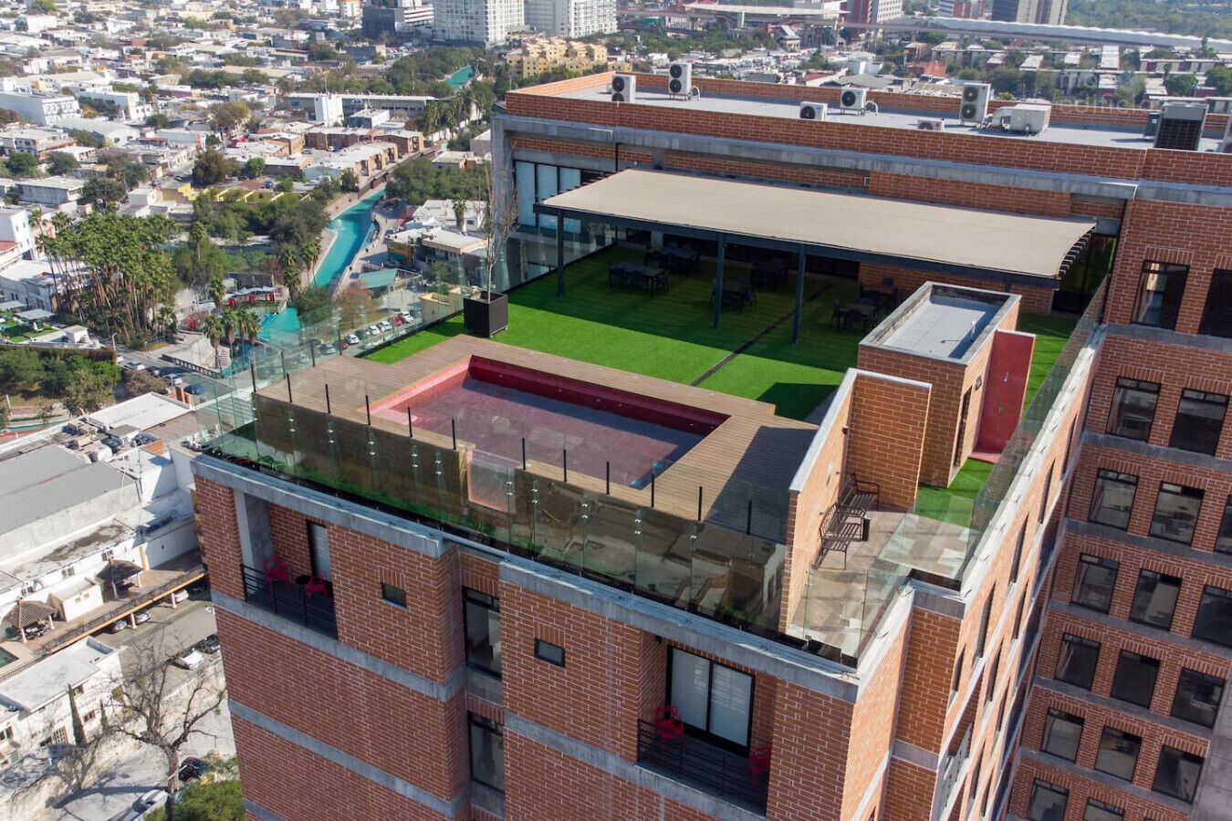 A high-rise building with a rooftop terrace featuring a pool, seating area, and a glass-enclosed space.