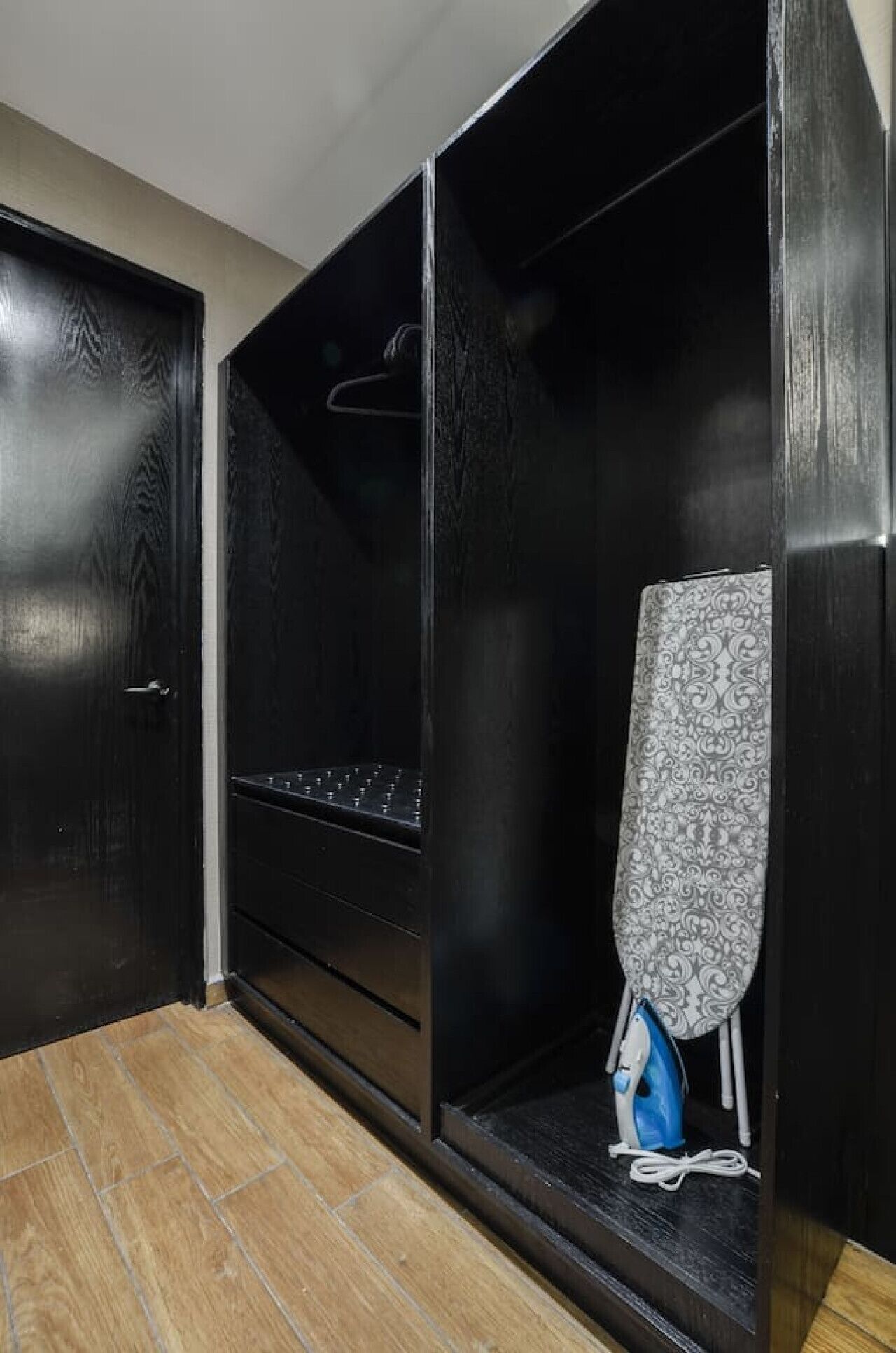 Un vestidor con barra para colgar, estantes y un planchado azul en el suelo.
