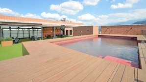 Uma área de piscina no terraço com deck de madeira, parede de tijolos e área de lounge envidraçada com assentos externos.