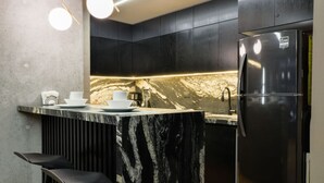 Cozinha moderna com ilha de mármore, armários pretos e geladeira de aço inoxidável.