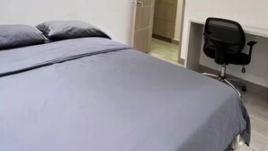 Ein modernes Schlafzimmer mit Bett, Klimaanlage, Schreibtisch mit Stuhl und einer Tür zu einem weiteren Raum.