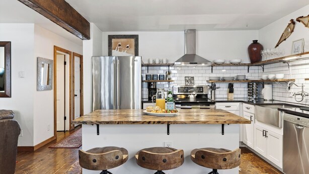 A modern kitchen with a central island, stainless steel appliances, and wooden stools.