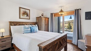 A bedroom with a wooden bed, a nightstand, a dresser, a chandelier, and a view of the outdoors.