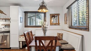 A kitchen with a dining area, a window with blinds, a hanging light fixture, and a radiator.
