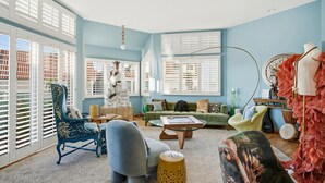 Ein geräumiges Wohnzimmer mit großem Fenster, einem grünen Sofa, einem blauen Sessel und einer dekorativen Statue.