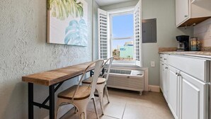 A kitchen with a wooden table, white chairs, a window with open shutters, and a view of buildings outside. - Beachview 321 Studio across from the Hangout (Gulf Shores)