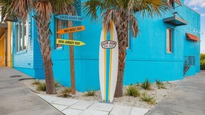 A blue building with palm trees, a surfboard, and directional signs. - Beachview 321 Studio across from the Hangout (Gulf Shores)