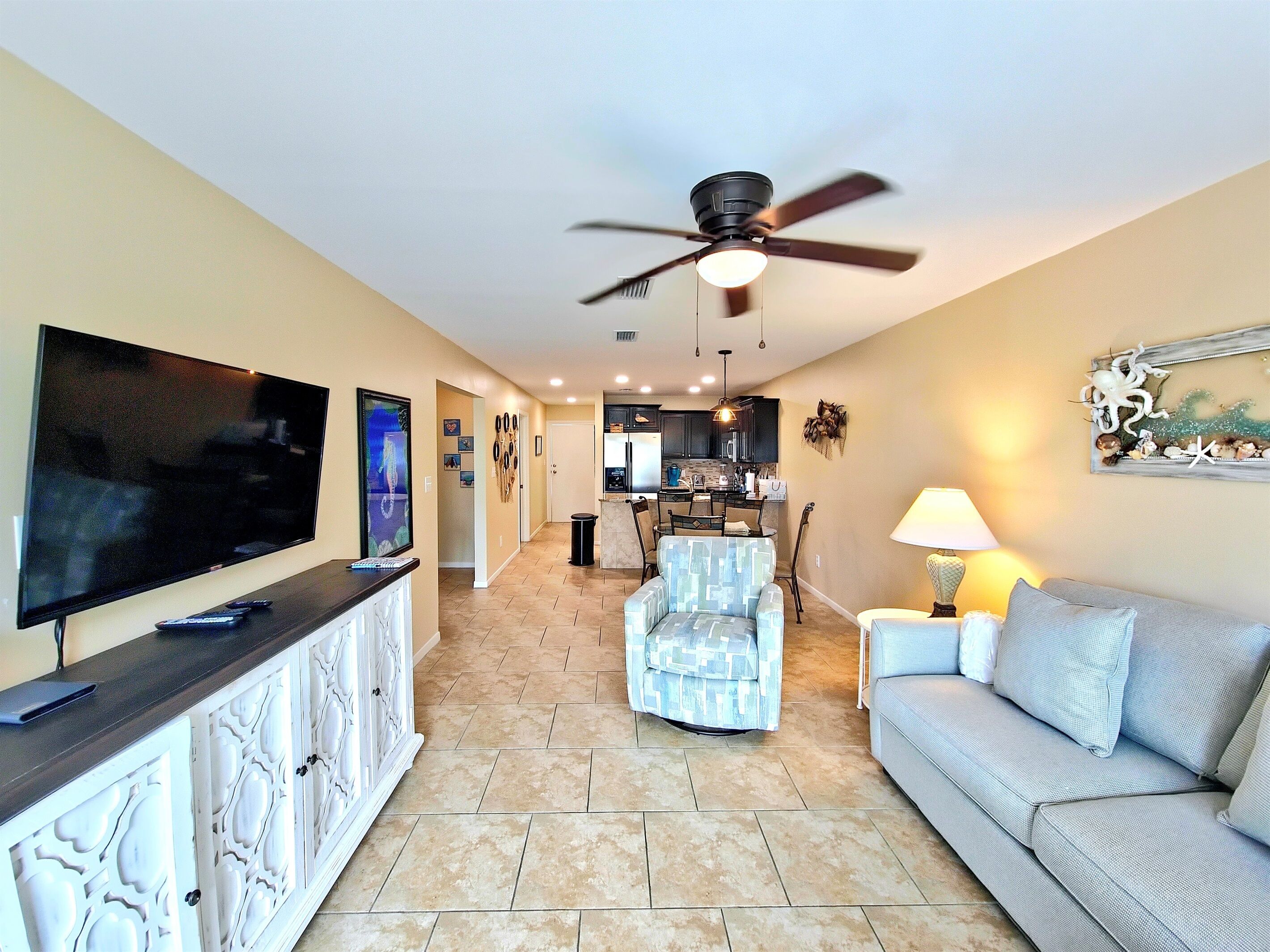 A living room with a TV, a ceiling fan, a sofa, and a dining area with a table and chairs.