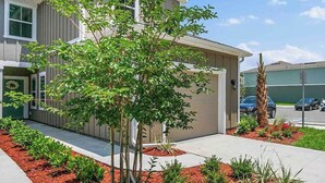 A modern two-story house with a well-maintained front yard, including a small tree and various shrubs. - Palm Villa: 5 beds Playground, UNF, Mayo, Downtown (Jacksonville)