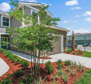 A modern two-story house with a well-maintained front yard, including a small tree and various shrubs. - Palm Villa: 5 beds Playground, UNF, Mayo, Downtown (Jacksonville)
