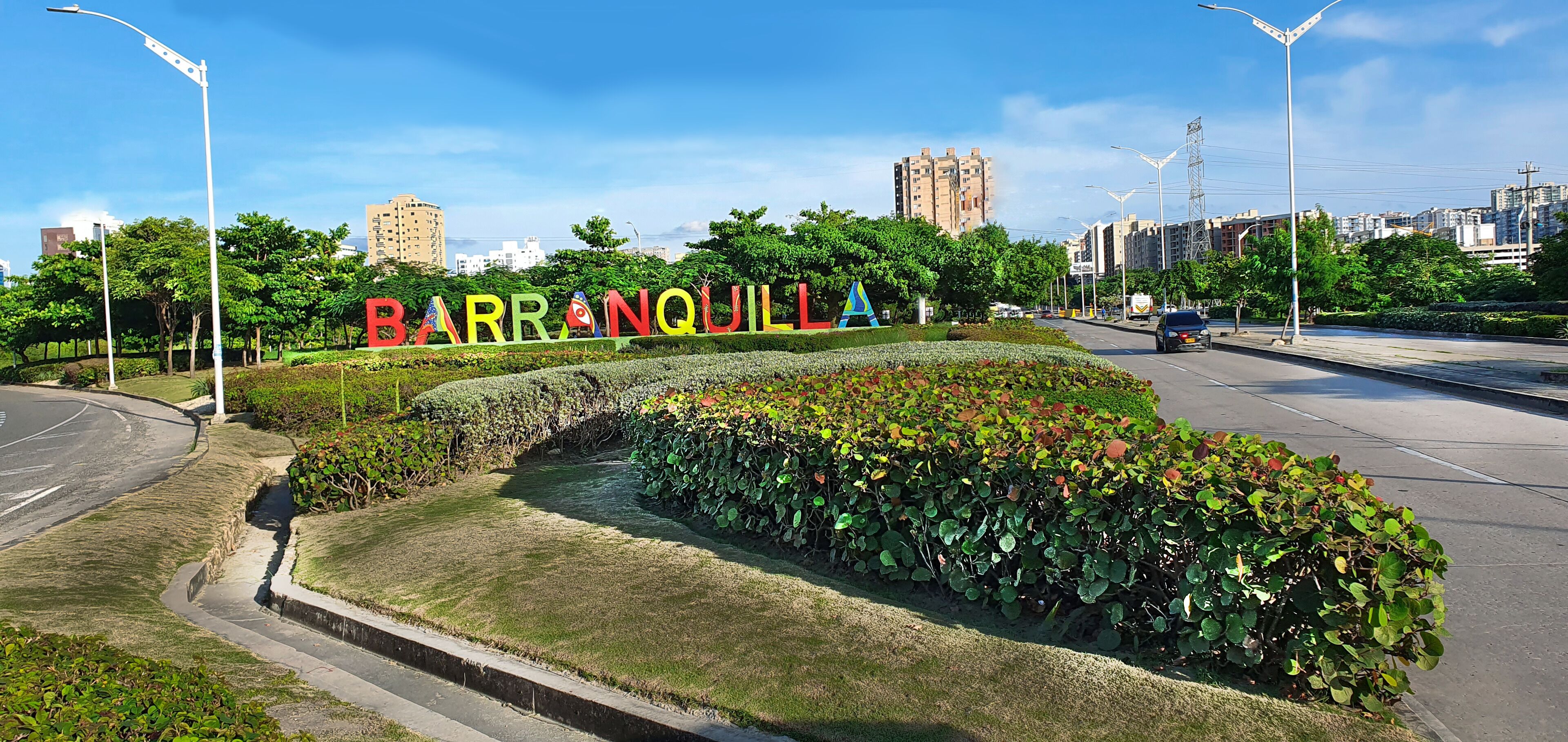 Uma área ajardinada com uma estrada, postes de luz e uma placa com a palavra 'BARRANQUILLA'.