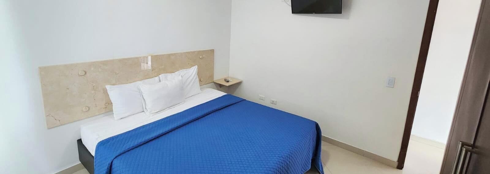 Un lit simple avec une tête de lit en bois, des oreillers blancs et une couverture bleue.