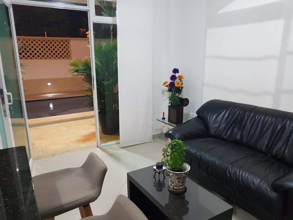 Una sala de estar moderna con un sofá de cuero negro, un ventanal de vidrio que da a un espacio exterior y una mesita con una planta.