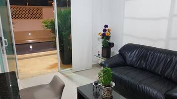 Una sala de estar moderna con un sofá de cuero negro, un ventanal de vidrio que da a un espacio exterior y una mesita con una planta.