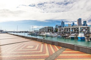 Ein Yachthafen mit vor Anker liegenden Booten, eine Stadtkulisse im Hintergrund und ein gemustertes Gehweg im Vordergrund.