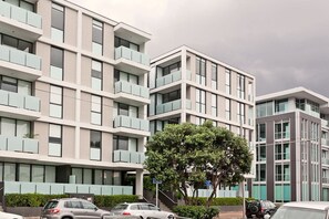 En flervåningsbyggnad med bostäder, balkonger, ett träd framför och parkerade bilar.