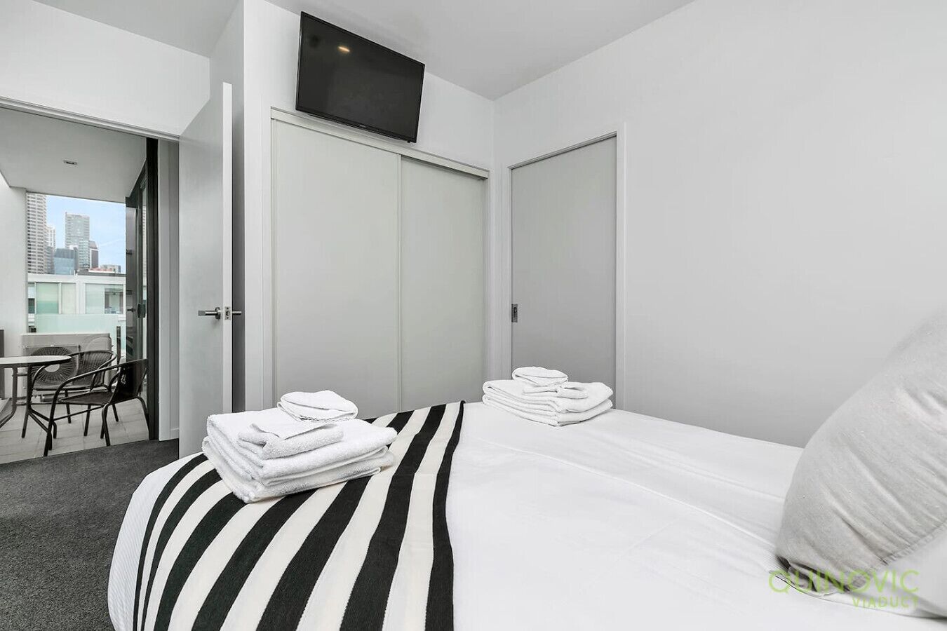 Habitación de hotel con cama, una silla, una mesa y balcón con vistas a la ciudad.