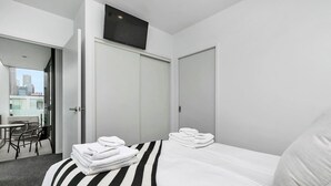 Habitación de hotel con cama, una silla, una mesa y balcón con vistas a la ciudad.