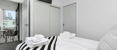 Habitación de hotel con cama, una silla, una mesa y balcón con vistas a la ciudad.