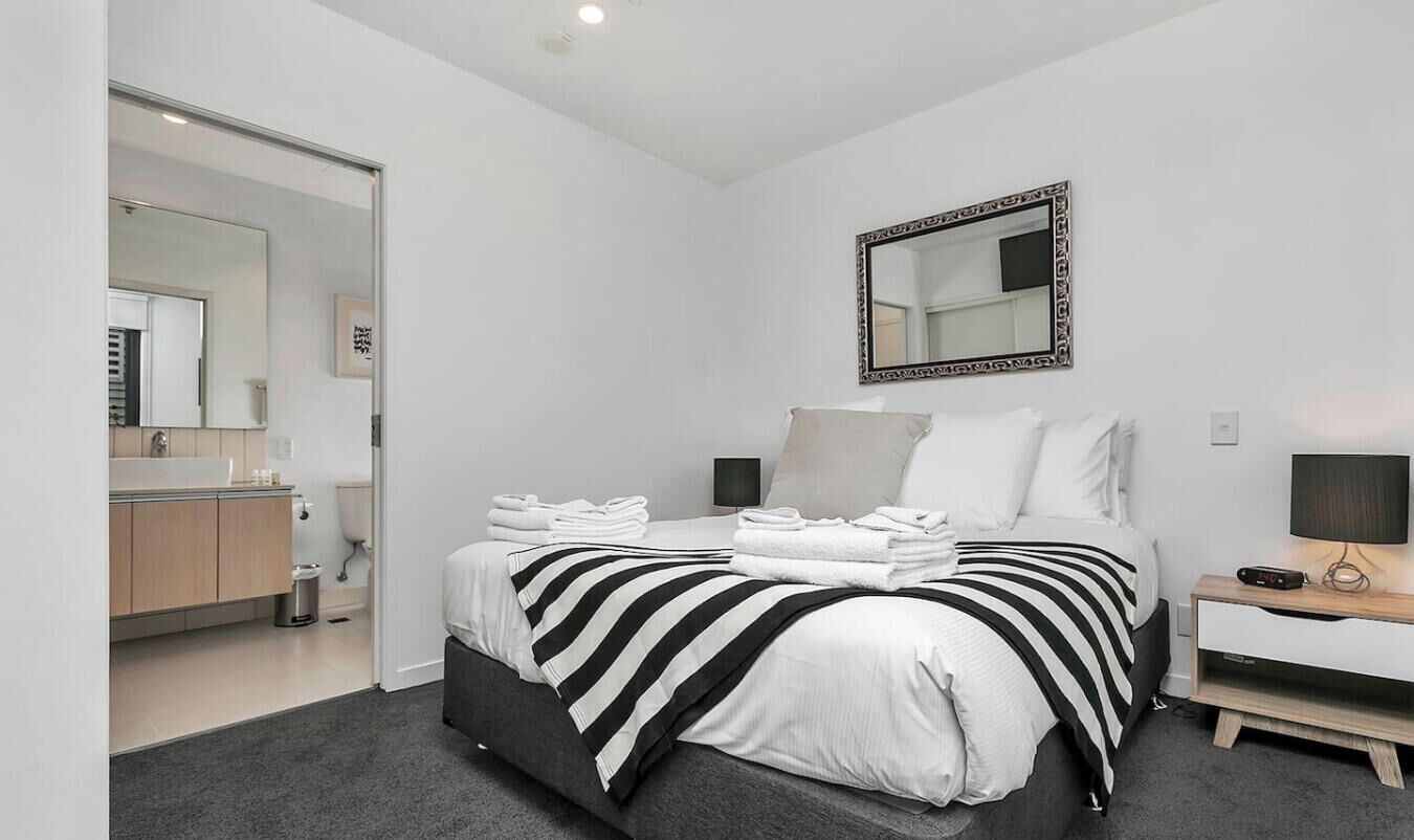 A bedroom with a bed, bedside table, and a mirror on the wall.