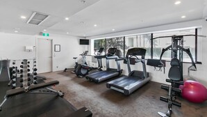 Un gimnasio con cintas de correr, máquinas de pesas y una pelota de ejercicios roja.