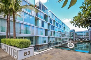 A modern hotel with a glass facade, a swimming pool, and palm trees. - Sophisticated 1 Bedroom Living with Parking (Auckland City)