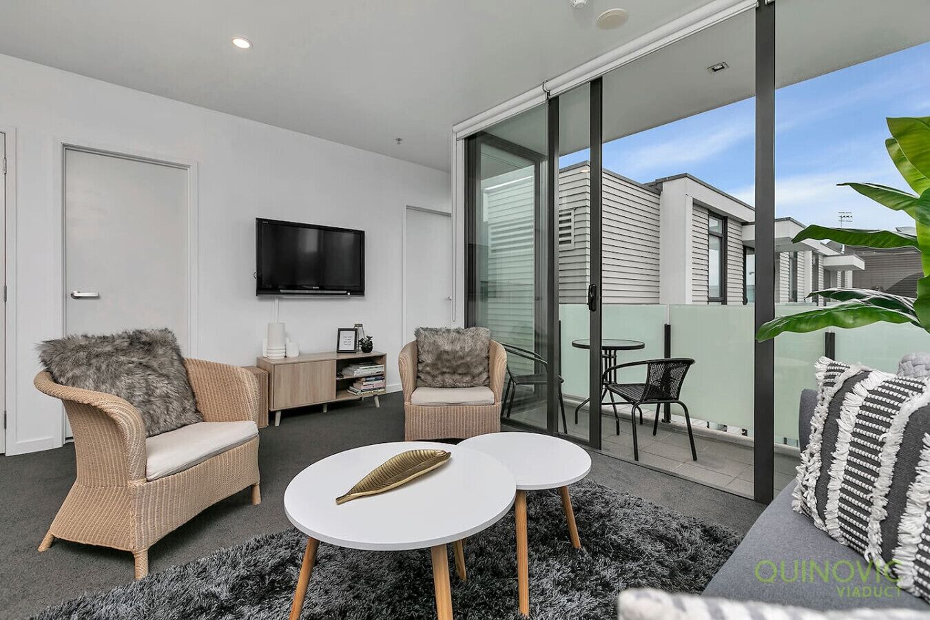 A modern living room with wicker furniture, a flat-screen TV, and a balcony with a table and chairs.