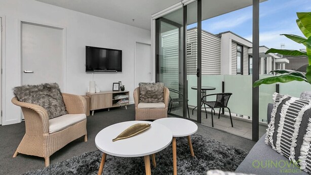 Una sala de estar moderna con muebles de mimbre, un televisor de pantalla plana y un balcón con mesa y sillas.
