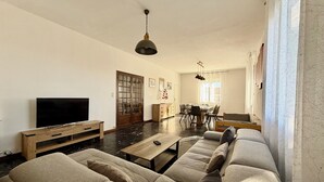 Una sala de estar con sofá, televisión, mueble de madera y una zona de comedor con sillas y mesa.