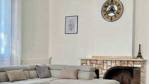 Una sala de estar con un sofá modular, una chimenea, un reloj y un cuadro en la pared.