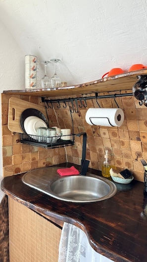 A kitchen with a wooden backsplash, a stainless steel sink, and a dish rack.