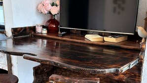 A rustic wooden bar area with a flat-screen TV, a vase of flowers, and a wooden stool.