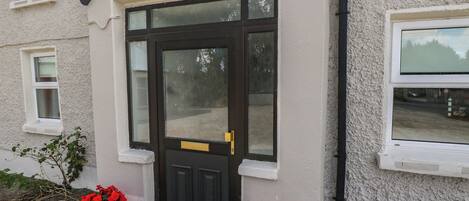 A building with a black front door, two potted red flowers, and a window on the right side.