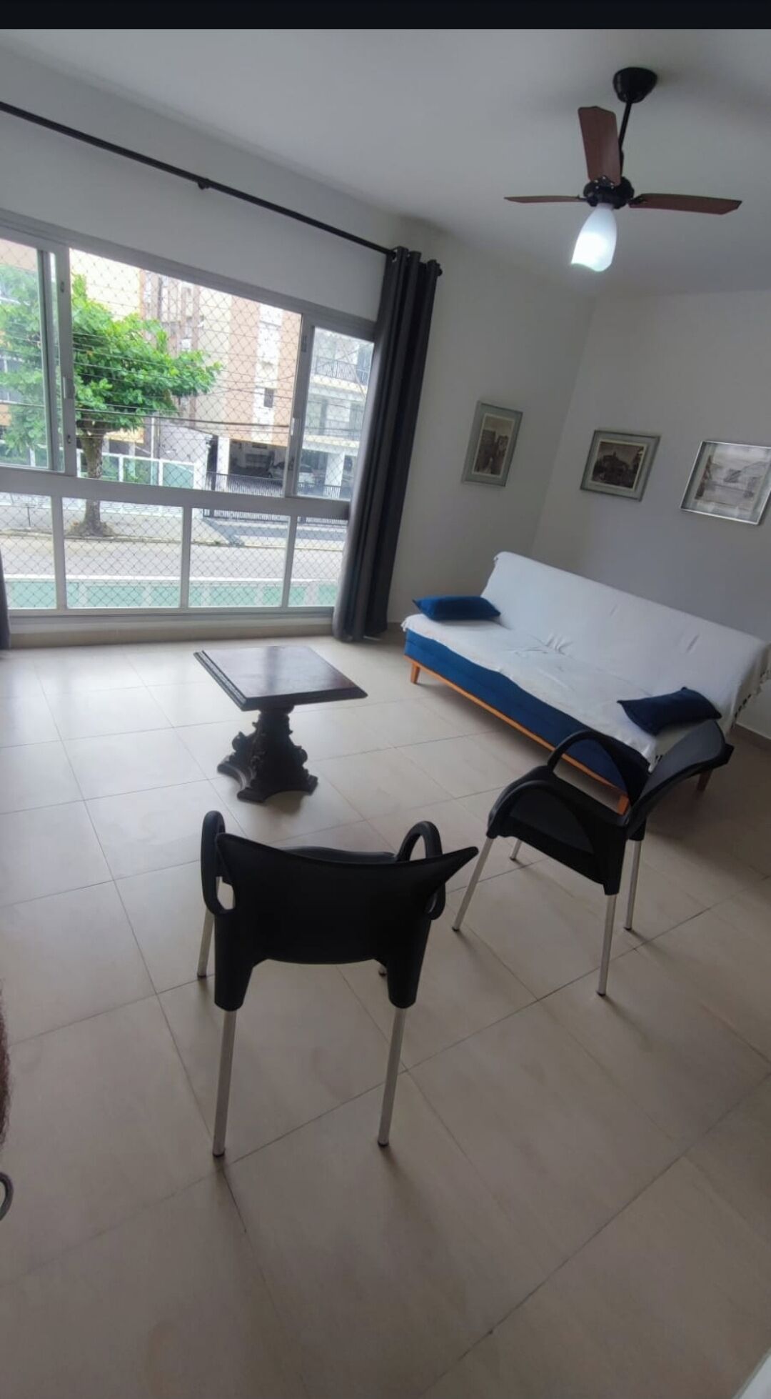 Une pièce comprenant un lit, une table, deux chaises, un ventilateur de plafond et de grandes fenêtres.