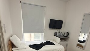 Una habitación pequeña y limpia con una cama individual, un escritorio con televisor y un espejo.