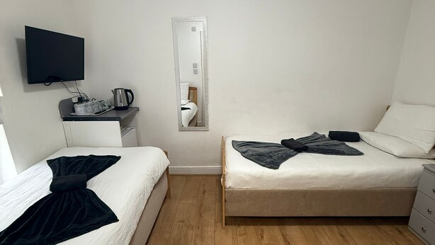 Habitación con dos camas individuales, un televisor de pantalla plana montado en la pared, una mesita con hervidor y un espejo.