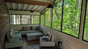 Una habitación acogedora con techo de madera, ventanas amplias, un sofá, una mesa baja y una pequeña mesa.