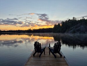 Een houten steiger met twee stoelen, gericht op een rustig meer bij zonsondergang.