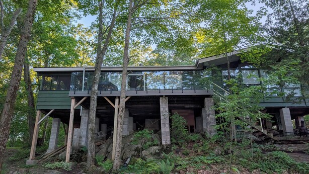 Una estructura moderna de madera con balcones de cristal, ubicada en un área boscosa.