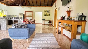 A spacious living area with a high ceiling, a kitchen in the background, and a television mounted on the wall. - Posada de Paz 1: A Family Refuge at Corcovado (Provincia de Puntarenas)