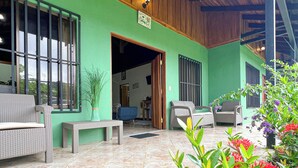 A covered outdoor area with a green wall, wooden ceiling, and tiled floor. There are outdoor furniture pieces and potted plants. - Posada de Paz 1: A Family Refuge at Corcovado (Provincia de Puntarenas)