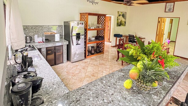 A kitchen with granite countertops, a refrigerator, and a dining area with chairs and a table. - Posada de Paz 1: A Family Refuge at Corcovado (Provincia de Puntarenas)