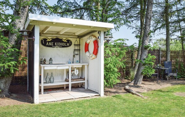 A small outdoor structure labeled "ANE KIDHOLM" with a lifebuoy, a shelf with bottles, and a bench.