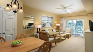 Habitación de hotel con una mesa de comedor, un sofá, un televisor y un balcón con vistas.