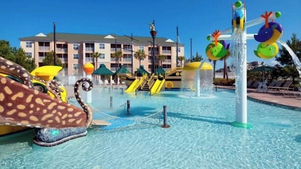 Parque acuático con toboganes y piscina, rodeado por un edificio con balcones.