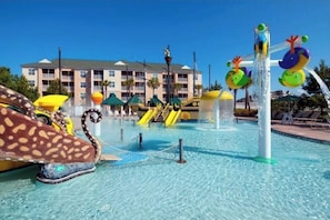 Un parc aquatique avec des toboggans et une piscine, entouré d’un bâtiment doté de balcons.